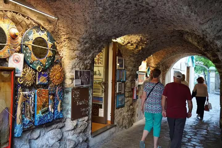 Tourists walk through historic stone archways adorned with art in Amalfi Coast's charming streets.