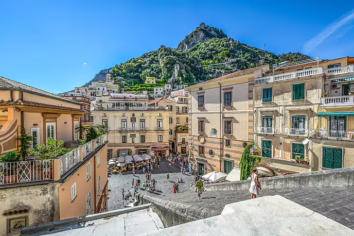 View over bustling Amalfi town square and pastel houses backed by lush coastal mountains on an Amalfi Coast & Ravello day trip