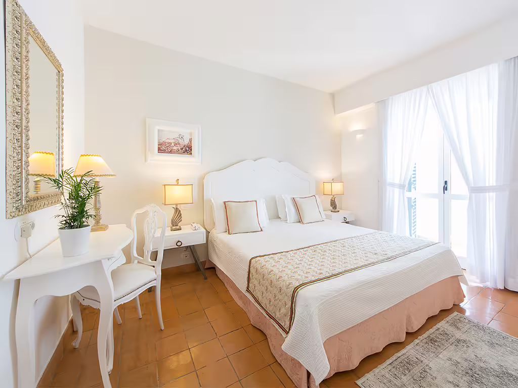 Bright Amalfi Coast hotel bedroom with king bed, soft white décor, balcony and natural light, ideal for a romantic spa escape