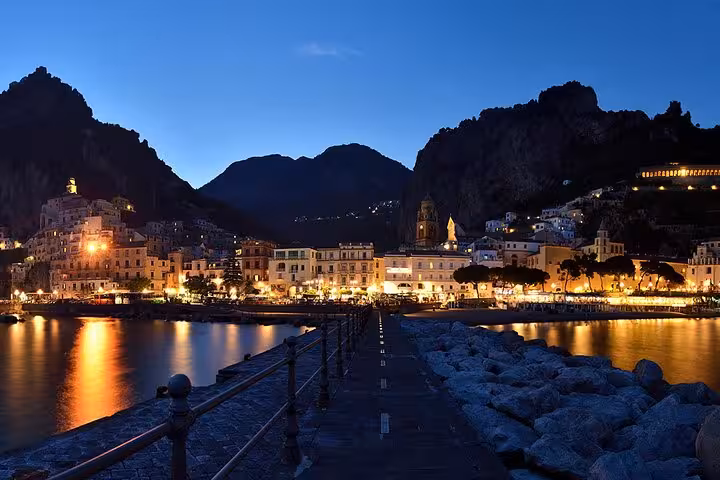 Charming Amalfi Coast town glowing at twilight with mountains silhouetted against the evening sky, ideal for night tours.