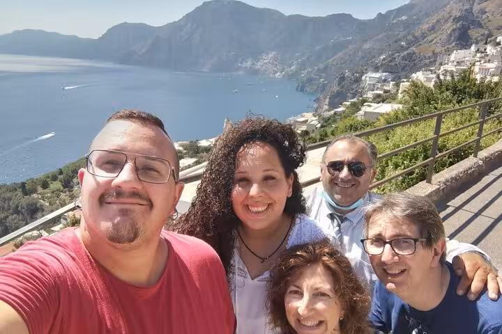 Group of tourists smiling with the stunning Amalfi Coast and blue sea in the background on a sunny day.