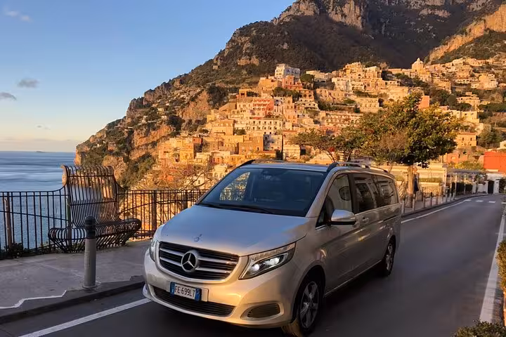 Mercedes van on a coastal road with a breathtaking view of Positano's colorful hillside, featured in an Amalfi Coast tour.