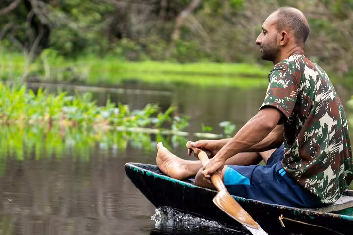 Man paddling a canoe through the tranquil waters of the Amazon rainforest, exploring the natural beauty of the area.