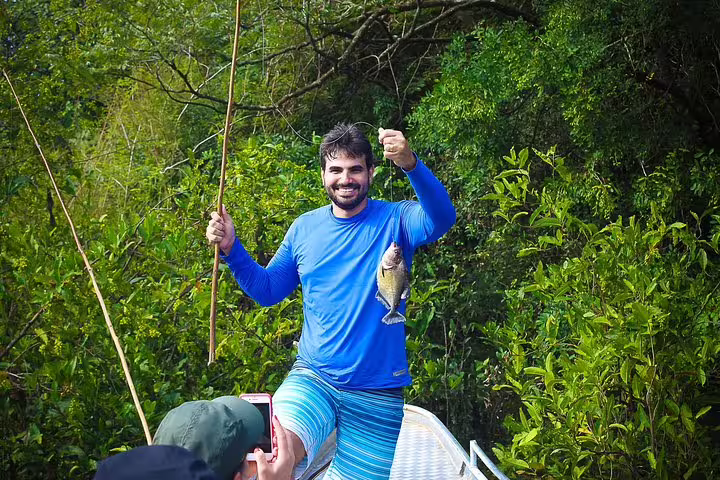 Smiling man in blue shirt proudly displays his catch during fishing expedition on Amazon survival adventure.