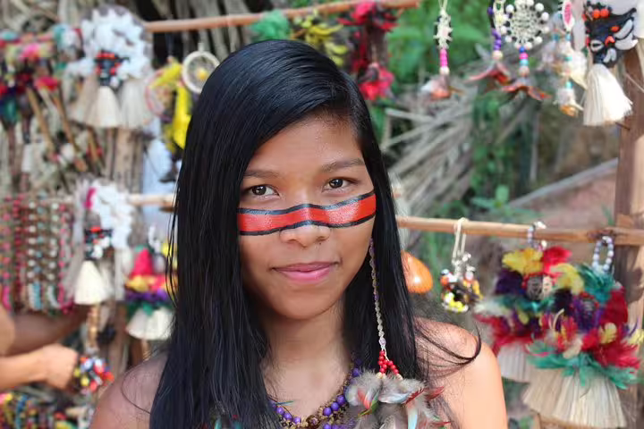 Indigenous artisan with traditional face paint and handmade jewelry at a cultural market in the Amazon rainforest.