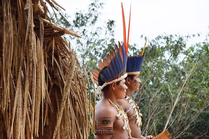 Two Amazon indigenous men in feather headdresses outside maloca during Indian Village and Meeting of the Waters tour