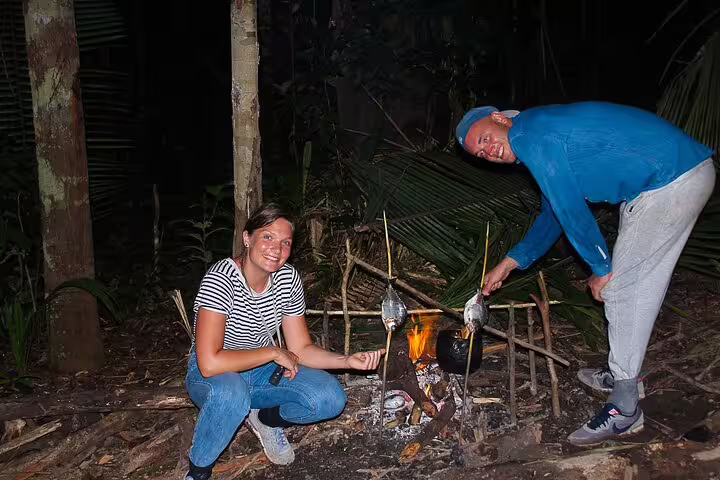 Adventurers cooking fish over an open fire in the Amazon jungle at night as part of the survival experience.