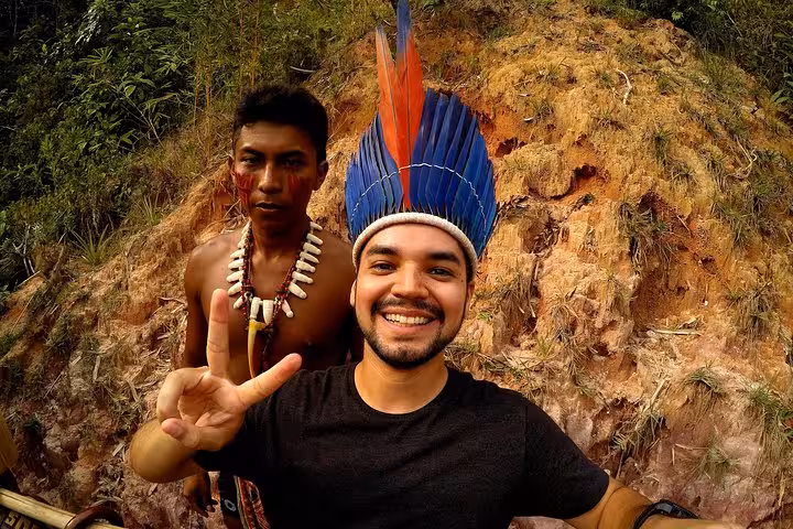 Tourist wearing indigenous feather headdress with local guide, cultural visit on 5-day Amazon jungle adventure tour