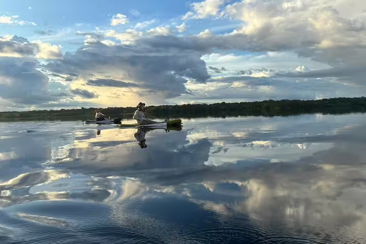 Kayakers paddle on serene Amanã Lake reflecting clouds, ideal for an Amazon survival tour.