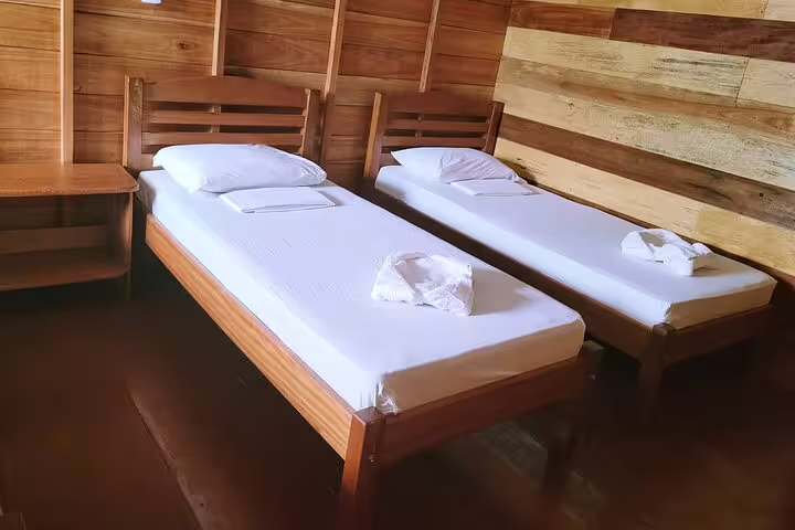 Cozy twin beds with crisp linens in a rustic wooden room at Amazon Tapiri Floating Lodge.