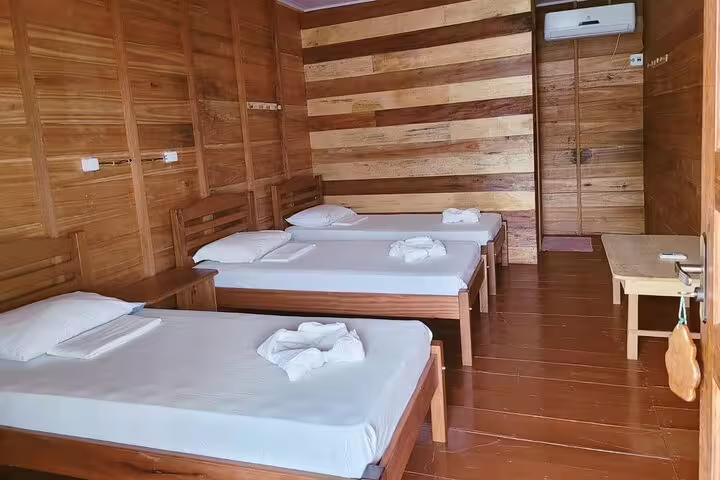 Cozy wooden room with three beds at Amazon Tapiri Floating Lodge, offering serene accommodation in the Amazon.