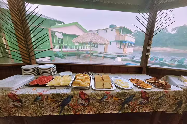 Table with fresh breakfast spread at Amazon Tapiri Floating Lodge, featuring fruits, bread, and scenic river views.