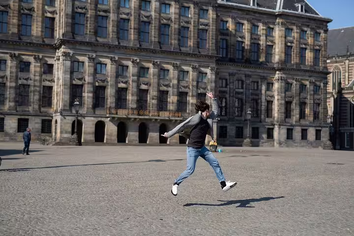 Person joyfully jumping in front of historic Amsterdam building during Amstagram Tour, capturing vibrant city exploration.