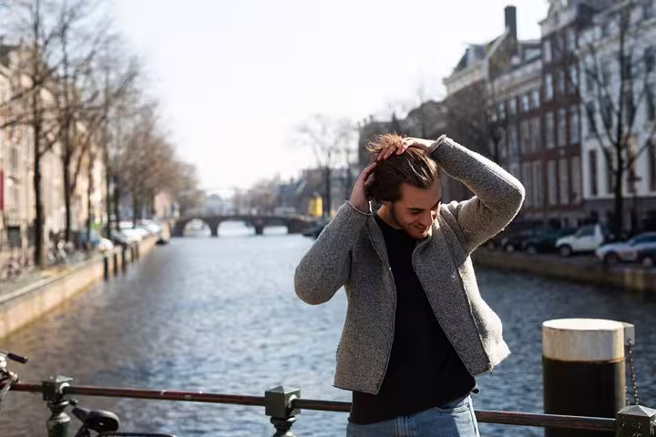 Person enjoying a sunny day by the Amsterdam canal during the Amstagram Tour & Moco Experience, surrounded by historic architecture.
