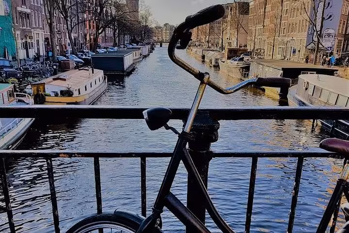 Bicycle on Amsterdam canal bridge overlooking houseboats and waterways, classic city tour view