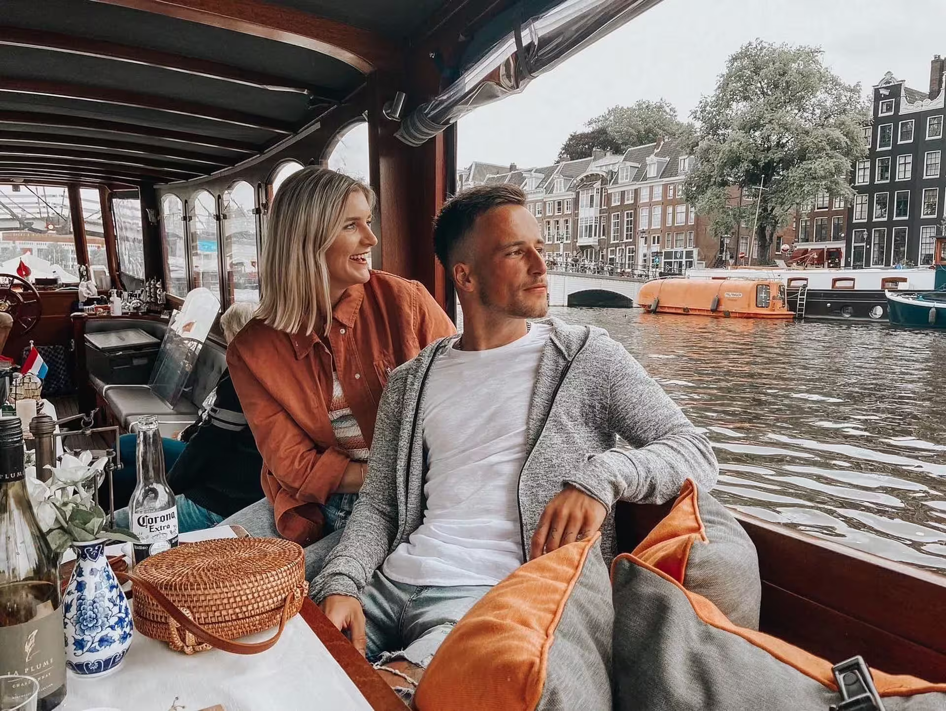 Couple enjoying Amsterdam canal cruise with drinks, cheese, and picturesque views, part of a guided bike tour experience.