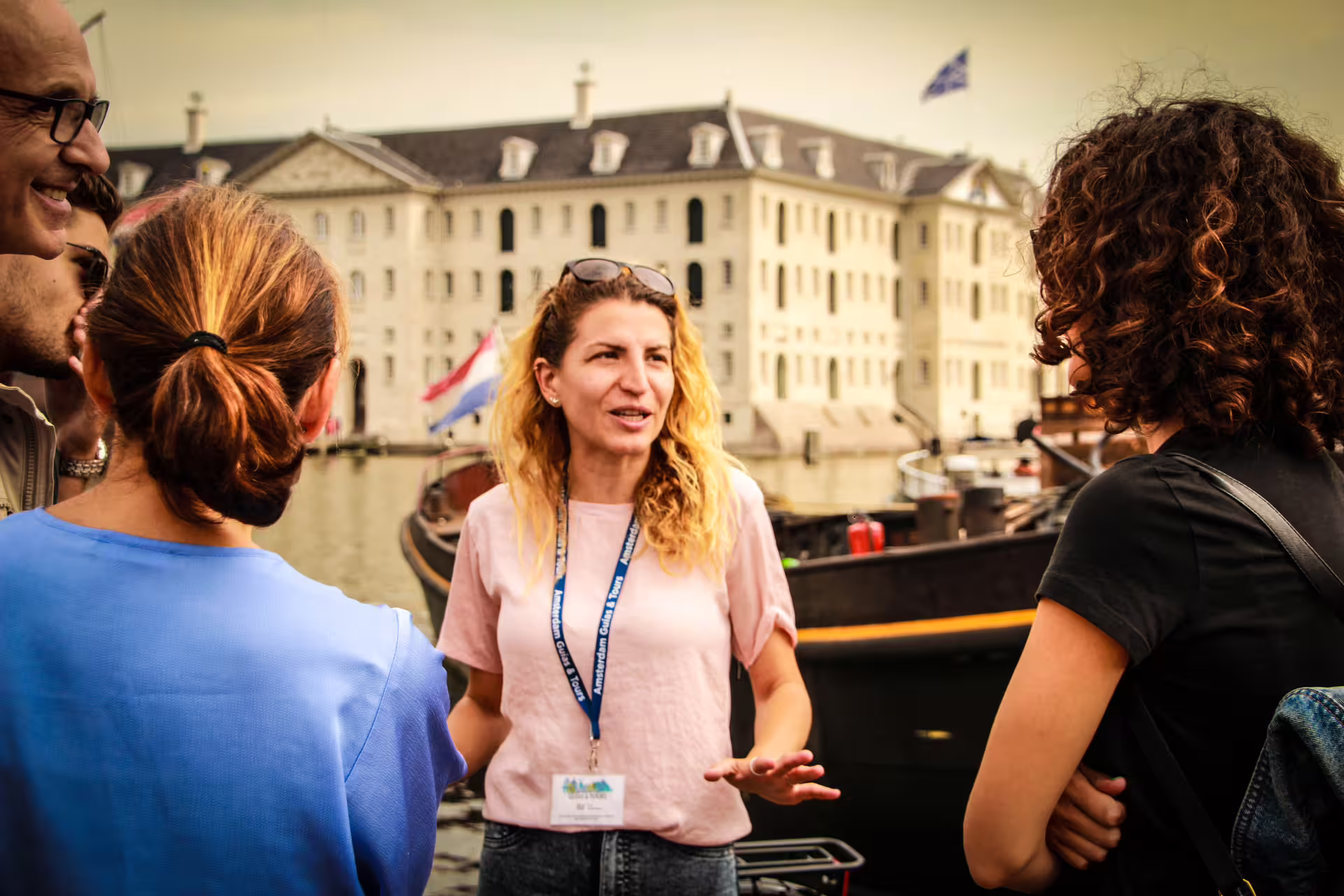 Tour guide engages a group by the Amsterdam canal, with historic buildings in the background, during a bike and cruise tour.