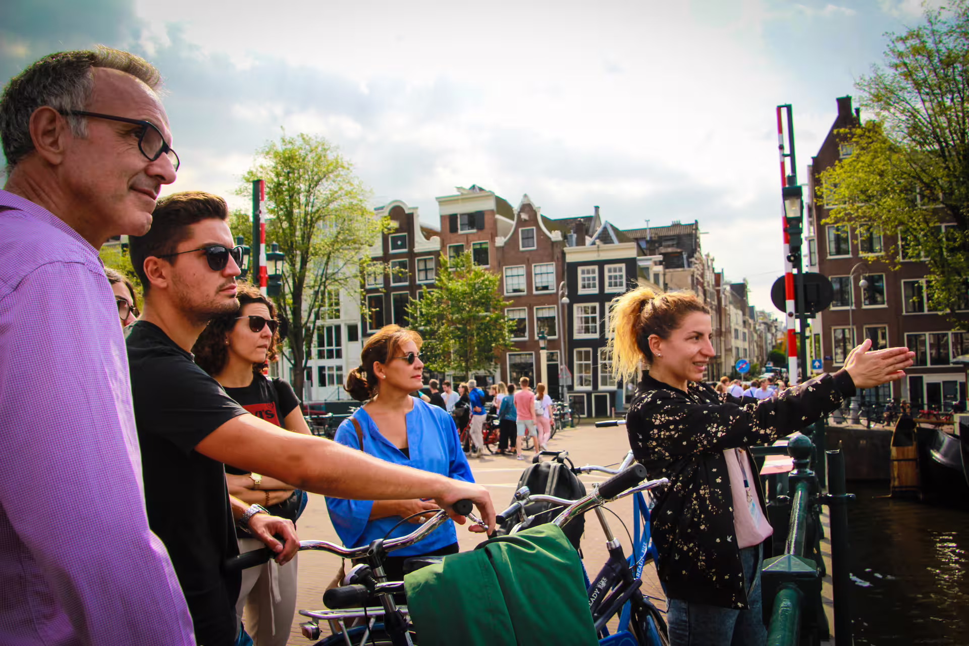 Small group enjoying an Amsterdam bike tour, exploring iconic canals and historic architecture under a sunny sky.