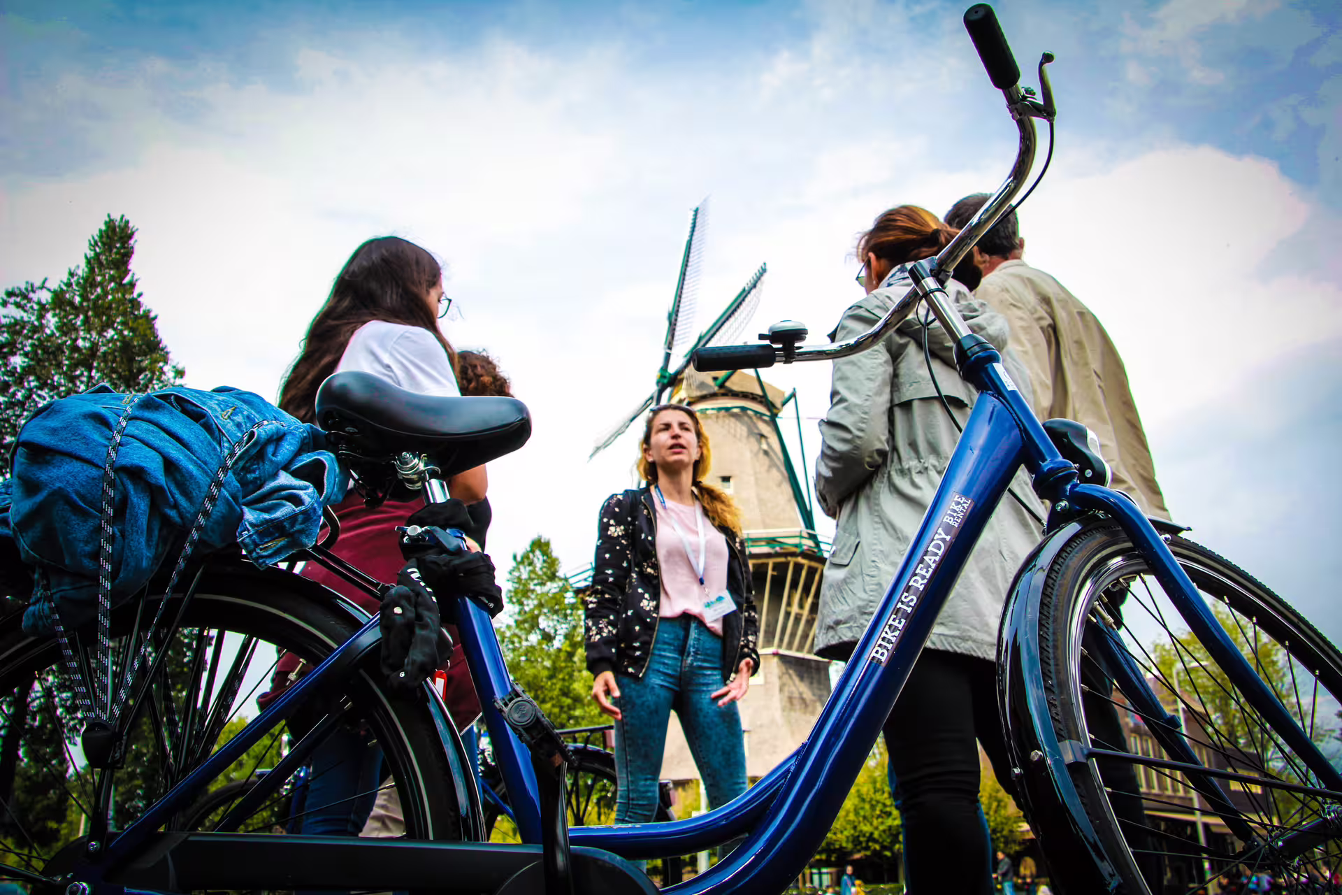Small group on Amsterdam bike tour stops near iconic windmill, highlighting Dutch culture and cycling adventure.