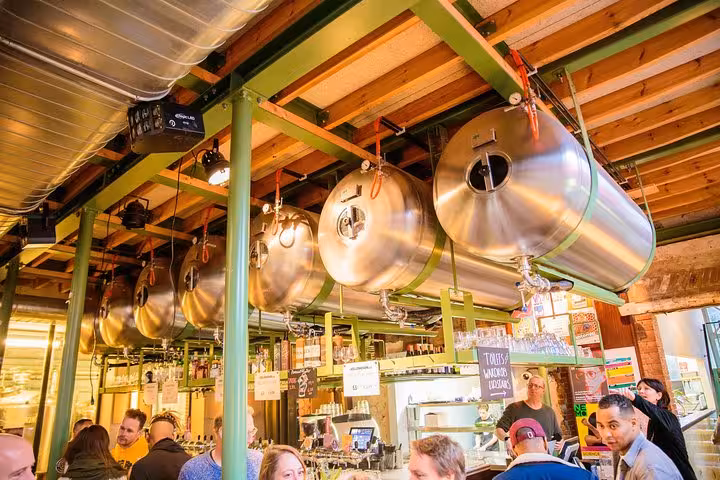 Amsterdam craft beer brewery tour stop with shiny fermentation tanks above a lively tasting room bar