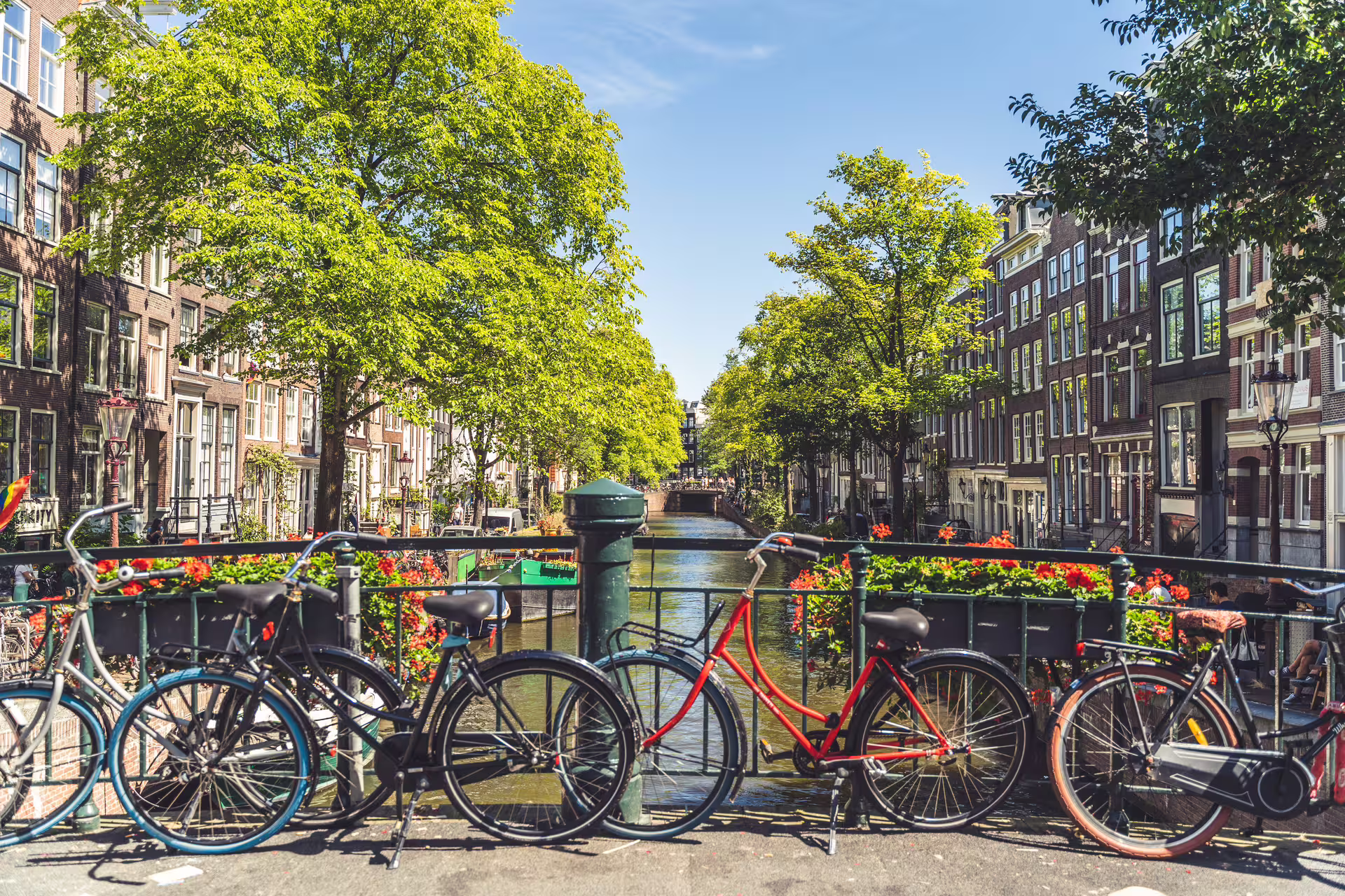 Bicycles on a picturesque Amsterdam canal bridge with vibrant flowers and historic buildings, ideal for walking and canal tours.