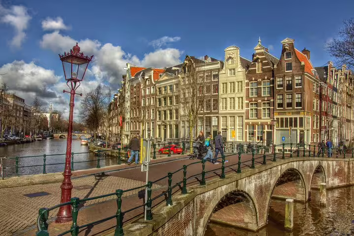 Cyclists crossing Amsterdam canal bridge by gabled houses, featured on a 19th century private guided bike tour