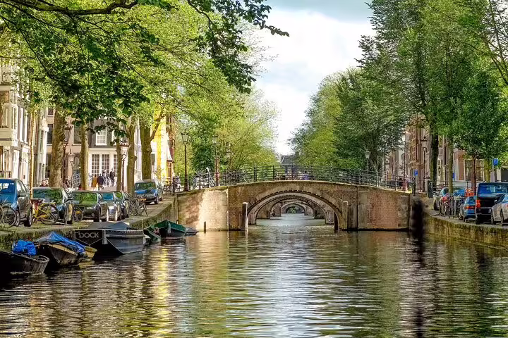 Tree-lined Amsterdam canal and arched bridge, scenic stop on a 19th century private guided bike tour