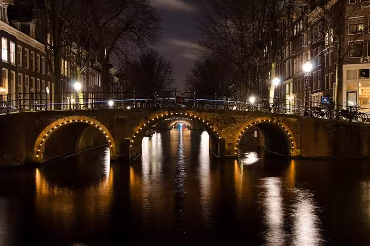 Amsterdam canal bridge at night with lights and reflections, ideal for private local transfer tour pickup