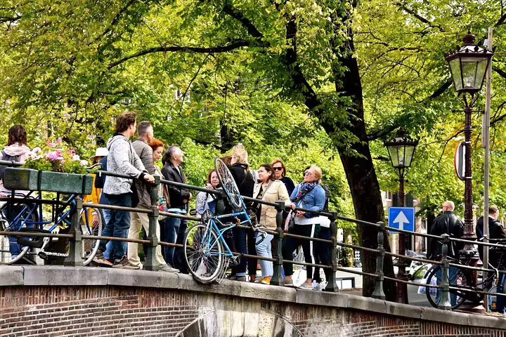 Travelers on a leafy Amsterdam canal bridge with bicycles, exploring secret spots on a private walking tour
