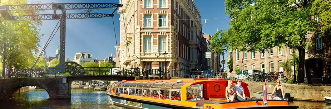 Vibrant canal cruise boat passing under a historic bridge with cyclists in Amsterdam, perfect for exploring the picturesque countryside.