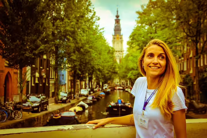 Smiling tourist enjoys Amsterdam walking tour with canal cruise, featuring unlimited drinks and cheese tasting by scenic waterways.