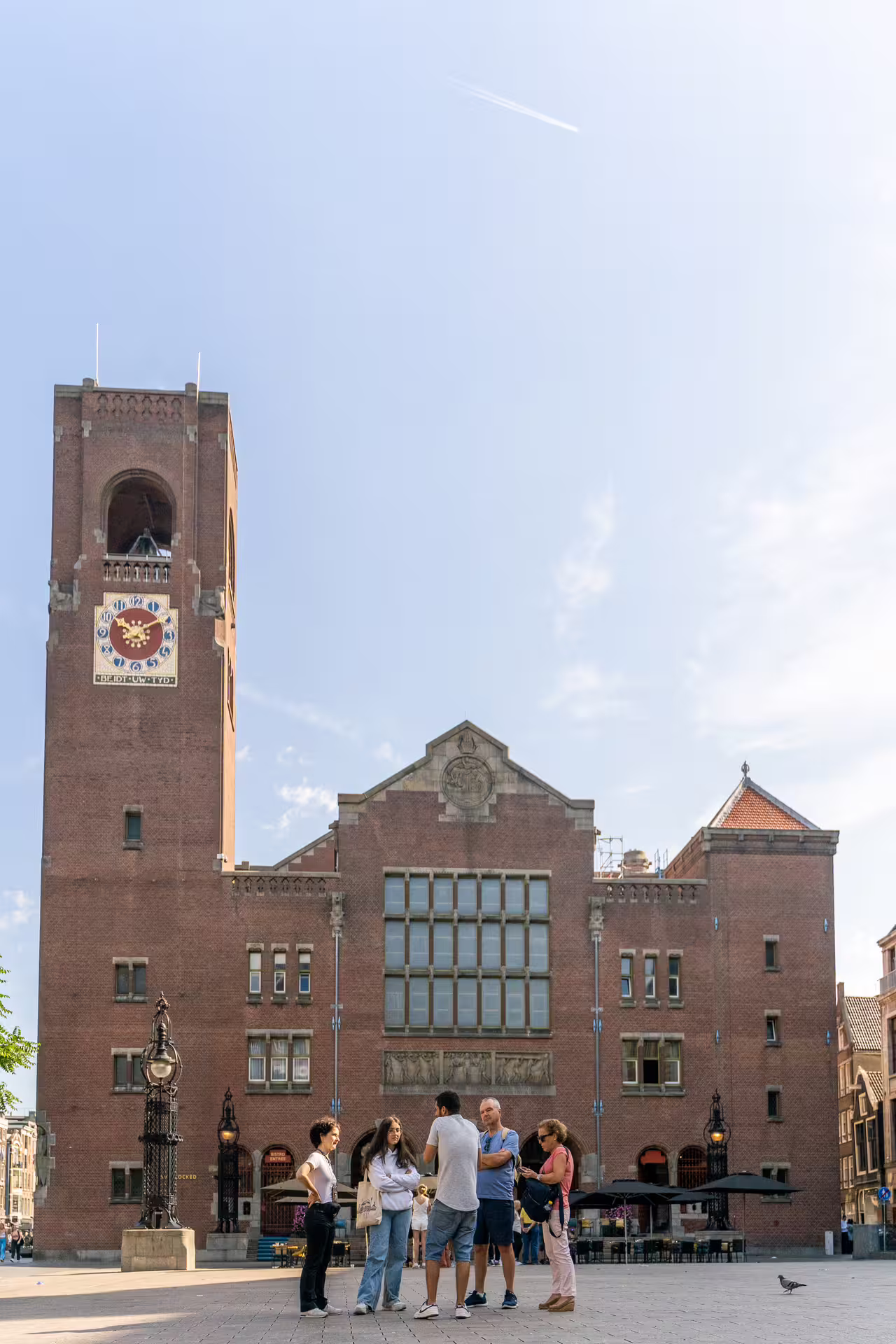 Group enjoying Amsterdam walking tour and canal cruise with unlimited drinks and cheese tasting by historic building.