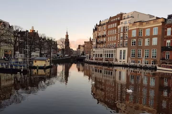 Amsterdam canal houses at sunset with calm water reflections, scenic city highlights on tour