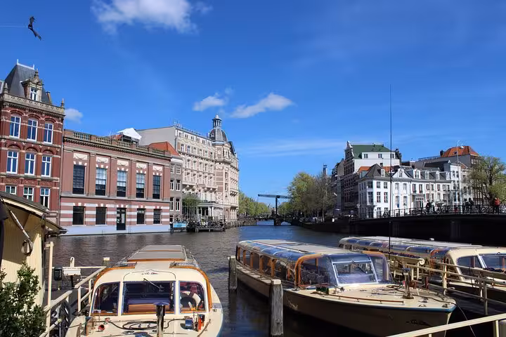 Canal-side Amsterdam architecture with moored boats under blue skies, ideal for a private local walking tour