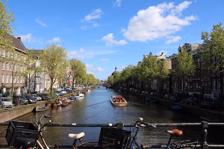 Amsterdam canal view from a bridge with bikes and a tour boat, perfect for a private local walking tour