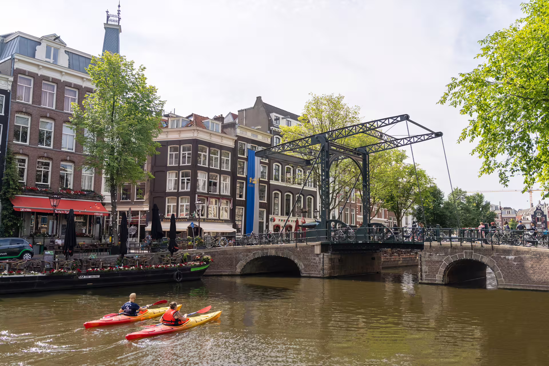Scenic Amsterdam canal view with kayakers, historic buildings, and a charming bridge, highlighting the walking tour and cheese tasting experience.