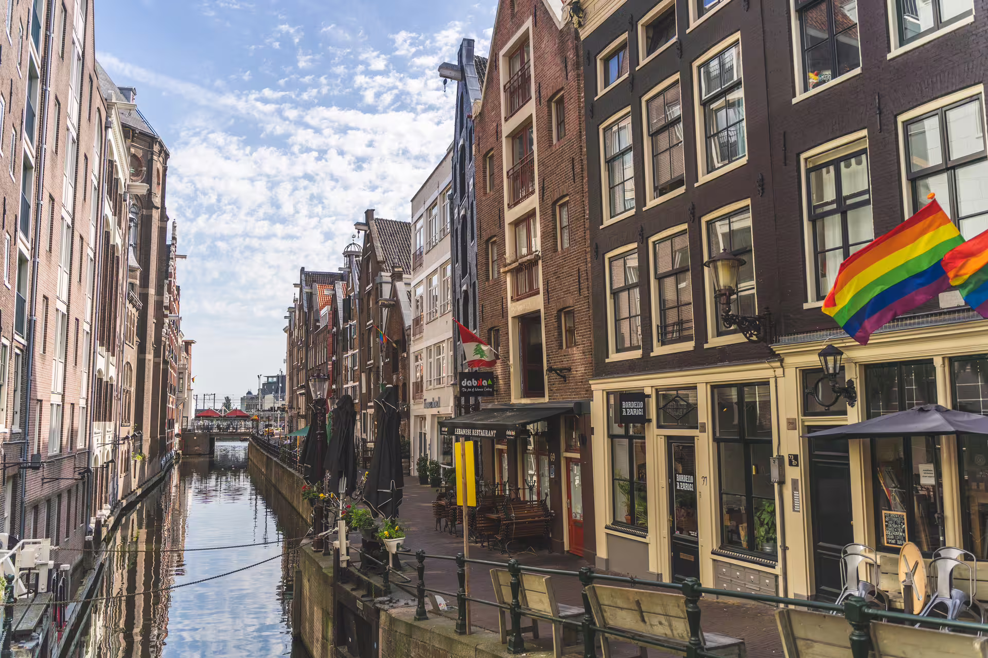 Charming Amsterdam canal scene with historic buildings and vibrant flags, perfect for a walking tour and cheese tasting adventure.