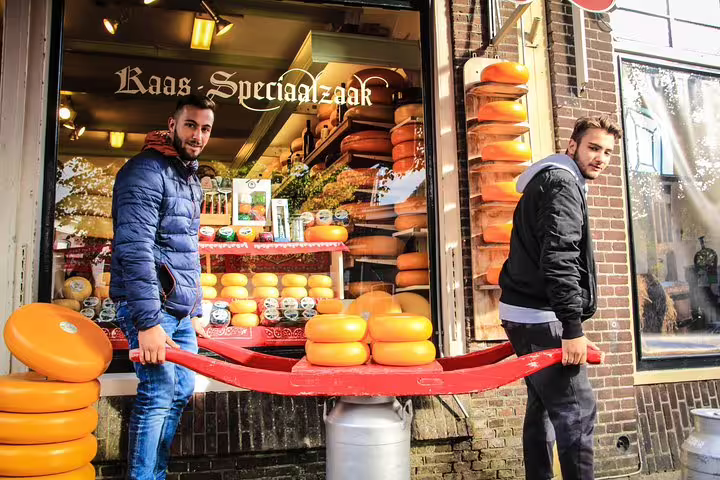 Two men carrying cheese wheels outside a traditional Amsterdam cheese shop, ideal for a walking tour with cheese tasting.
