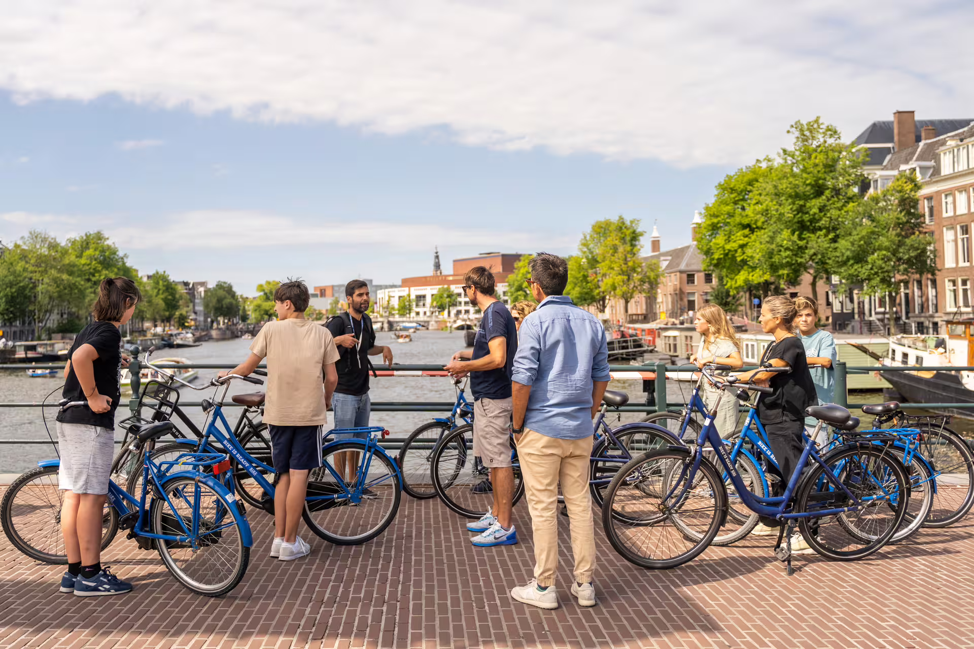 Group of tourists with bikes on a sunny day, exploring Amsterdam's scenic countryside, with a canal view in the background.