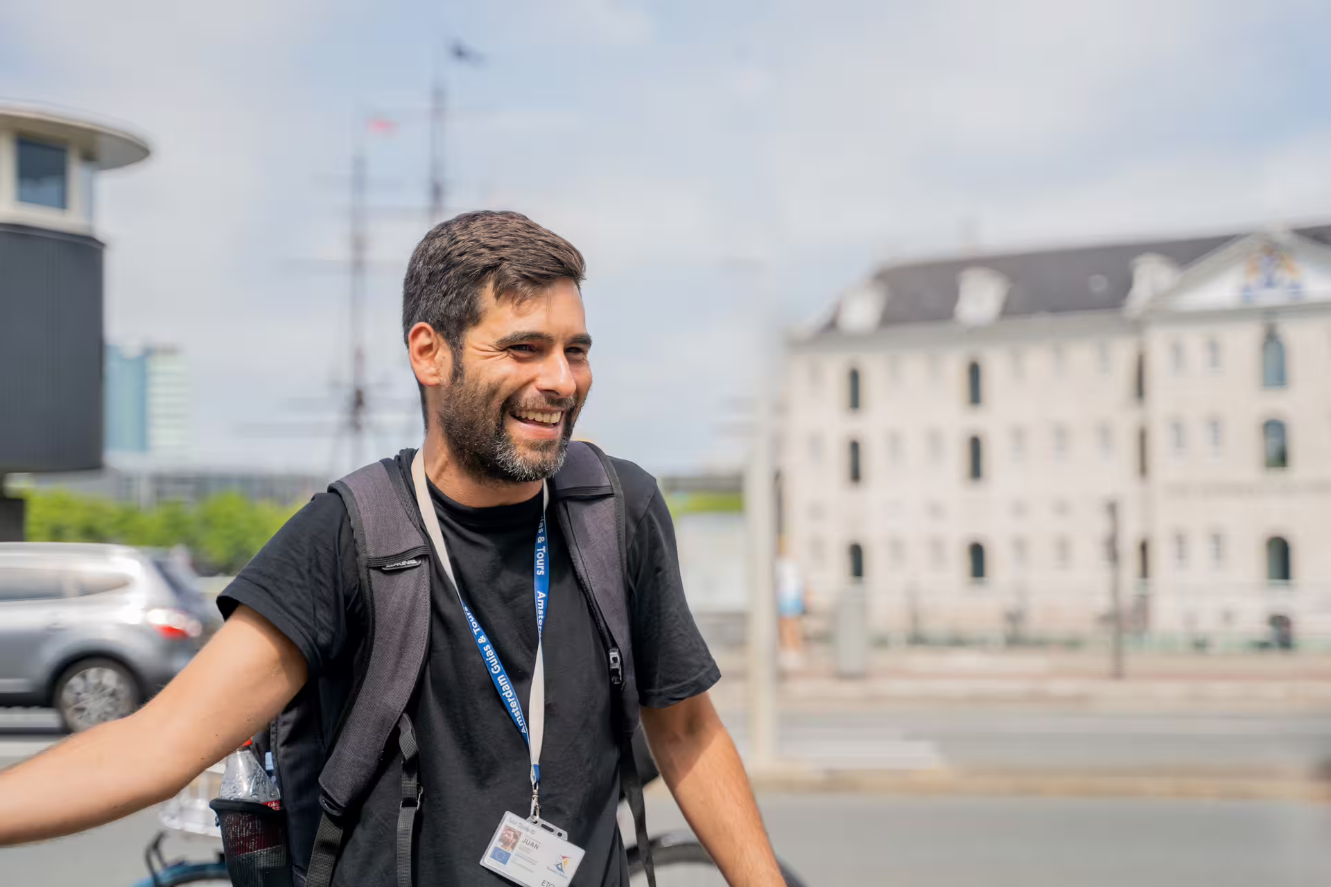 Smiling tour guide with a backpack and lanyard, ready to lead a scenic countryside bike tour, enhancing outdoor adventure experiences.