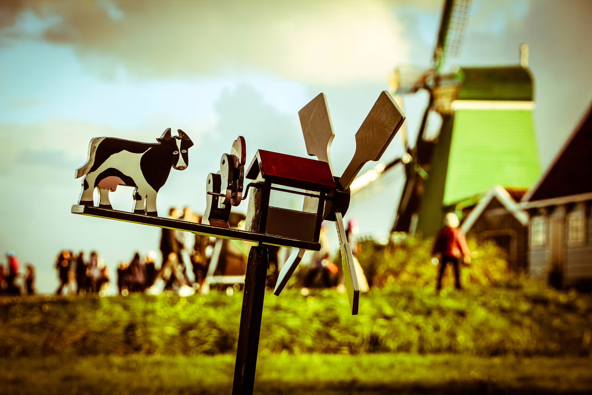 Close-up of a decorative cow and windmill in the Amsterdam countryside, with tourists in the background enjoying a bike tour.