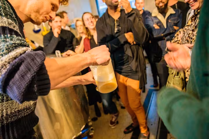 Guide pours fresh craft beer during Amsterdam brewery tour by bus, with tasting group watching in taproom