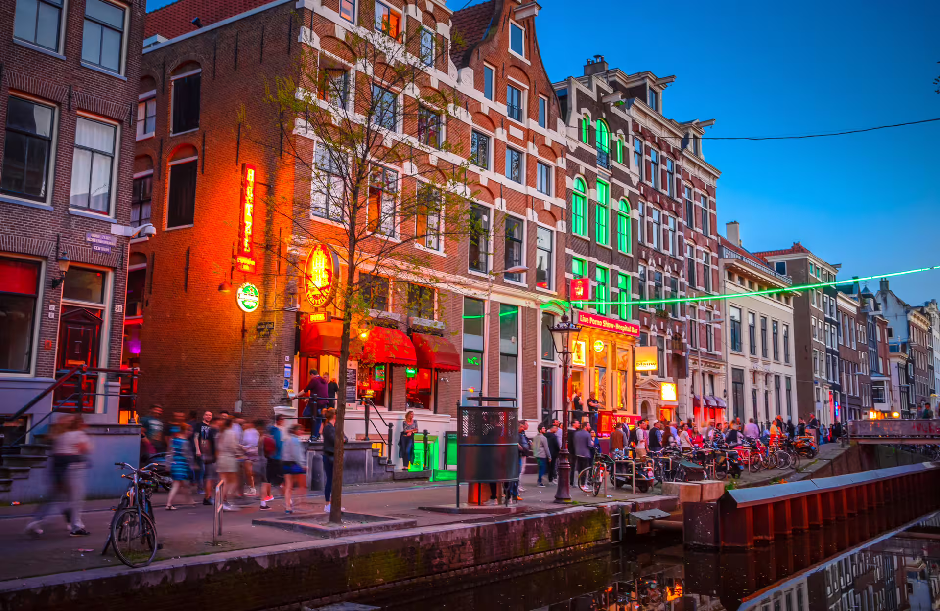 Evening crowds and neon along Amsterdam Red Light District canal, featured on 1-day walking tour audioguide