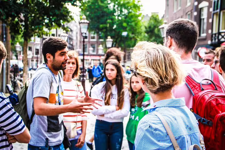 A tour guide leads a group through Amsterdam's historic streets, part of a walking tour and canal cruise with cheese tasting.