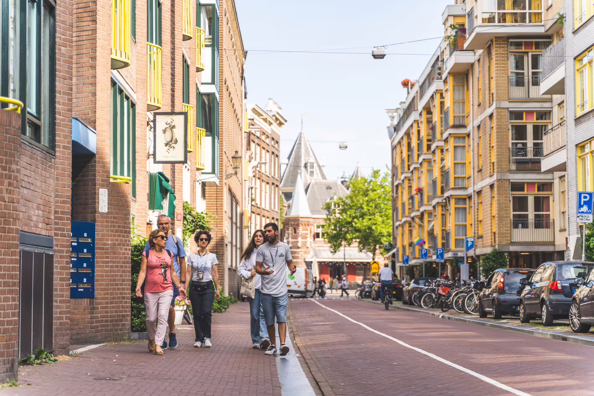 Tourists casually stroll through a charming Amsterdam street, surrounded by historic architecture, during a walking tour with canal cruise.