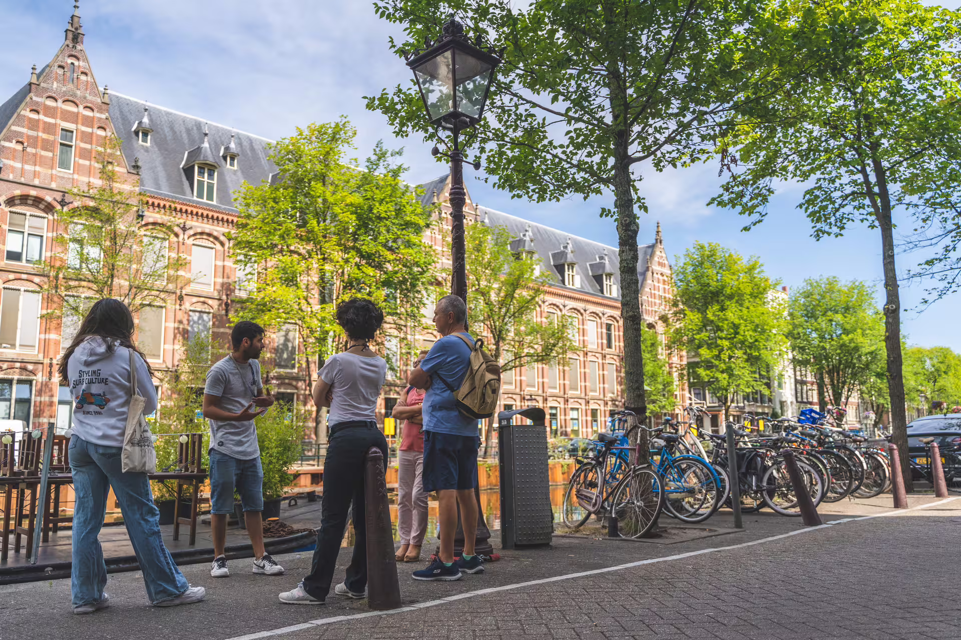 Group of tourists exploring picturesque Amsterdam street with historic architecture and bicycles, perfect for walking tours and canal cruises.