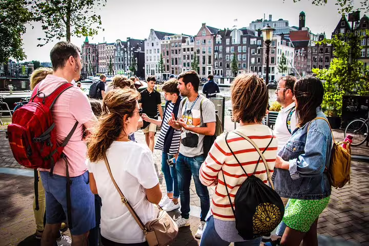 A group of tourists listens to a guide during an Amsterdam walking tour with scenic canal views and cheese tasting experience.