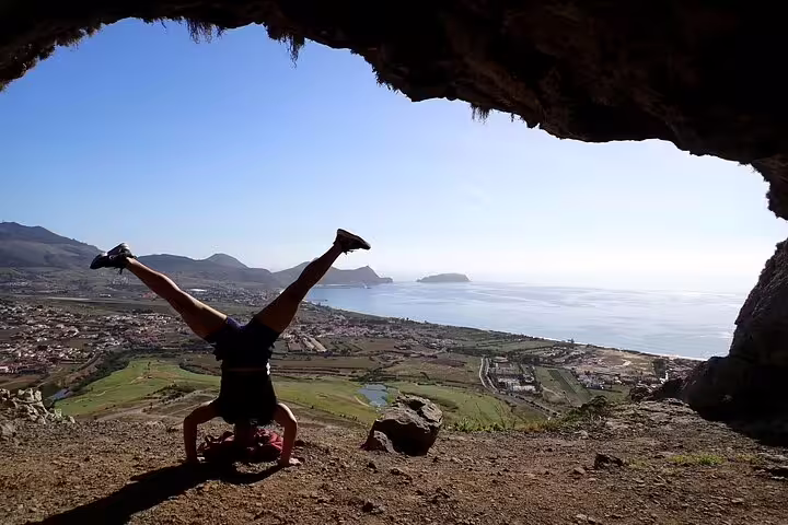 Adventurer performs a headstand in Ana Ferreira Cave, offering breathtaking views of the coastal landscape and peaks beyond.