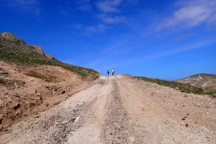 Hikers traverse a rugged dirt path under a vibrant blue sky on the scenic Ana Ferreira Caves & Peaks Trek in Madeira.