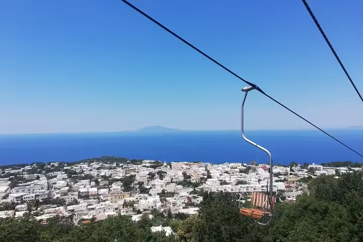 Chairlift offering panoramic views of Anacapri's whitewashed buildings and the azure sea stretching to the horizon.